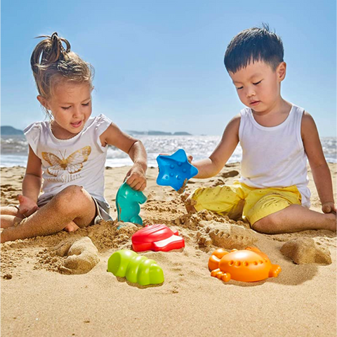 Boy and girl sitting on the sand at the beach playing with Hape sand toys