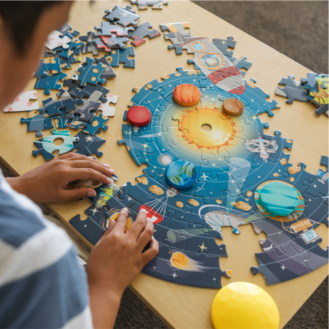 Young boy assembling at space themed circular puzzle. 