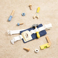 A Classic World Tool Belt from Classic World rests on a beige carpet, ready to inspire imaginative play. This set features a white belt with a blue pouch that holds a hammer. Scattered around the belt are various children's carpentry tools, including a toy wrench, ruler, screws, nuts, and bolts in coordinating shades of blue, yellow, and natural wood.
