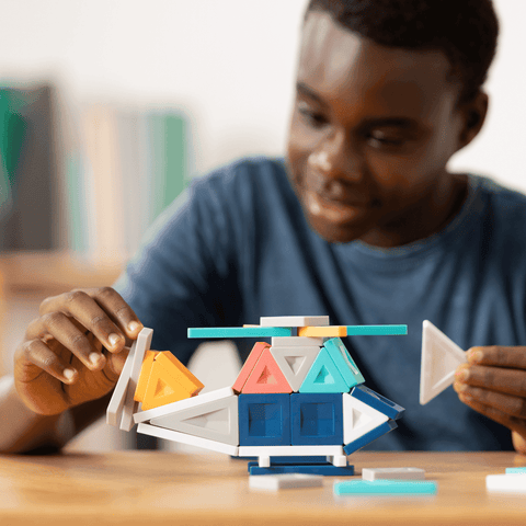 Child playing with colorful geometric building blocks on a wooden table.