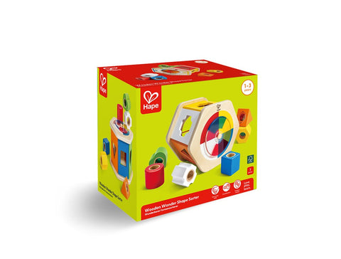 The image features a green box containing the HAPE Wooden Wonder Shape Sorter toy for ages 1-3. The packaging showcases vibrant images of the toy, highlighting various geometric shapes and a shape-sorting cube designed to enhance hands-on learning and cognitive development. The HAPE logo is prominently displayed at the top left and bottom front of the box.