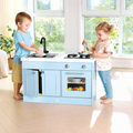 Two children standing and playing with the Hape Deluxe Kitchen with Running Water wooden play kitchen