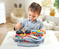 Child playing with a Hape Little Racer's Busy Board in a bright room.
