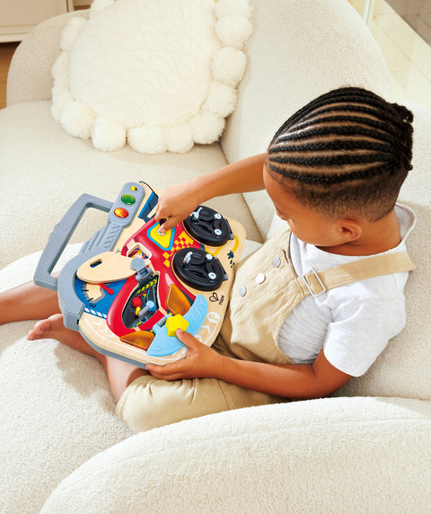 Child playing with a Hape Little Racer's Busy Board on a white couch