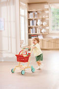 Child playing with a Hape Little Shopper's Cart & Basket in a bright room with wooden furniture.