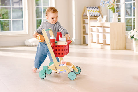 Child playing with a Hape Little Shopper's Cart & Basket in a home setting