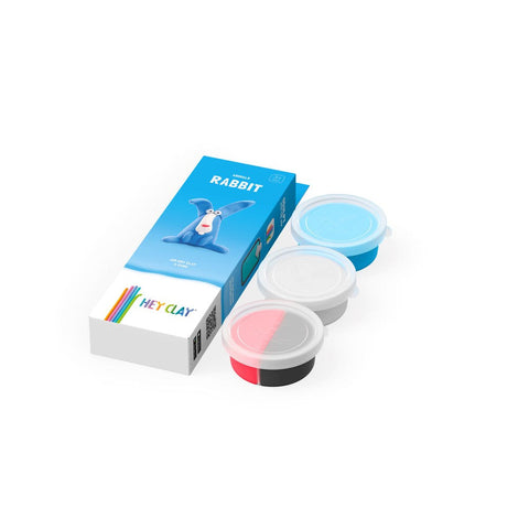 A set of modeling clay, including three round containers in blue, white, and red, is displayed next to packaging labeled "Hey Clay Single Pack - Rabbit" by Hey Clay. The package features a playful blue rabbit illustration and promotes play-based learning with vibrant colored pencils on the box.