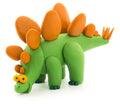The Hey Clay Single Pack - Stegosaurus by Hey Clay features a green, clay-like stegosaurus model with an orange backplate and spikes on its tail. It stands on four legs and sports large yellow eyes with black pupils and a smiling expression, making it perfect for play-based learning.