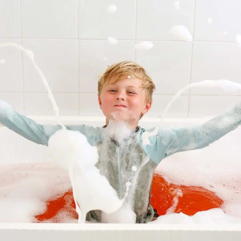 Child in a bathtub filled with bubbles and water, enjoying a bath.