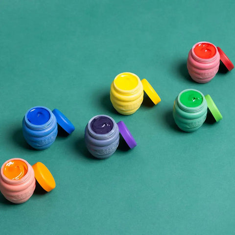 Colorful small jars with lids on a green background