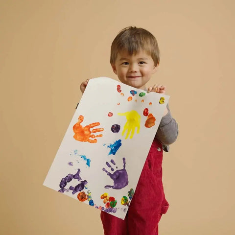Child holding a sheet of paper with colorful handprints against a beige background