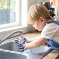 Child washing hands with adult supervision in a kitchen sink.