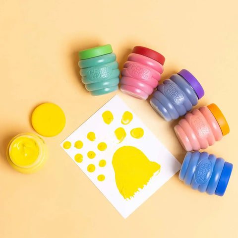 Colorful paint pots with a yellow paw print template on a beige background