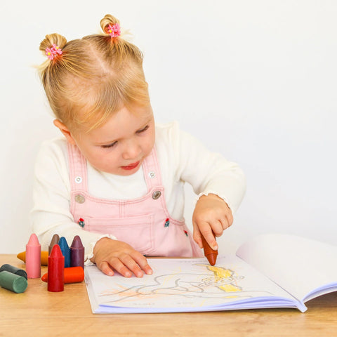 Toddler colouring in an animal outline in the Honeysticks Toddler's First Colouring Book, with a row of Honeysticks crayons beside the open book
