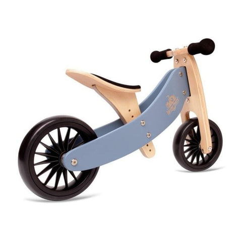 The Kinderboard Tiny Tot Plus - Slate Blue is a wooden 2-wheel balance bike with a slate blue frame, black padded seat, and black handlebars. It features two black wheels with multiple spokes and an adjustable seat height. The minimalist design is ideal for young children learning to balance.