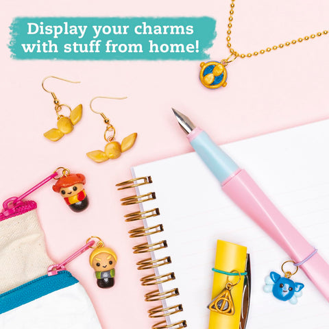 A flat lay featuring various themed charms from the Klutz Harry Potter Clay Charms collection, including a pair of earrings, a charm bracelet, and keychains attached to a zipper pouch. Arranged with common household items like a spiral notebook alongside pink and blue pens, the text on the image reads "Display your charms with stuff from home!