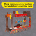 The Klutz Harry Potter Clay Charms drying rack, designed as a cardboard model of the Hogwarts Express train, is perfect for hanging your charm jewelry. Featuring whimsical charms such as a pie, a yellow shape, and a potion bottle made from polymer clay, this rack captures the enchantment of the Harry Potter series. The text at the top encouragingly states, "Hang charms on your custom Hogwarts Express drying rack.