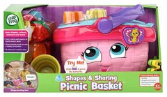 Image of the Leapfrog Shapes & Sharing Picnic Basket toy. The package features a pink basket with a smiling face, as well as colorful plastic food items and tableware. The box emphasizes interactive elements such as a talking picnic set and educational learning songs for children. Suitable for ages 6 months and up.