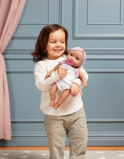 Child holding a Lullababy doll against a blue paneled wall