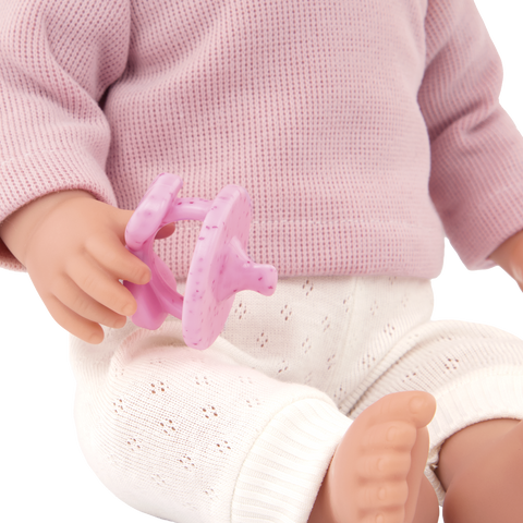 Close-up of a Lullababy doll wearing a pink sweater and white pants, holding a pink toy.