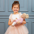 Young girl in a pink dress holding a Lullababy doll against a blue paneled wall