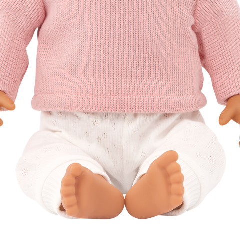 Close-up of a Lullababy doll wearing a pink sweater and white pants with a white background