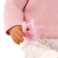 Close-up of a Lullababy doll's hand holding a pink pacifier against a pink sweater background