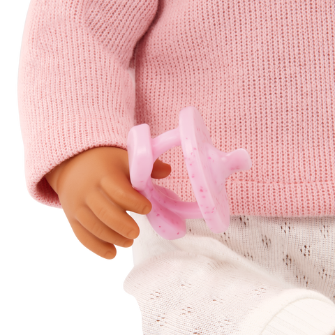 Close-up of a Lullababy doll's hand holding a pink pacifier against a pink sweater background
