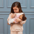 Young girl holding a Lullababy doll against a blue paneled wall