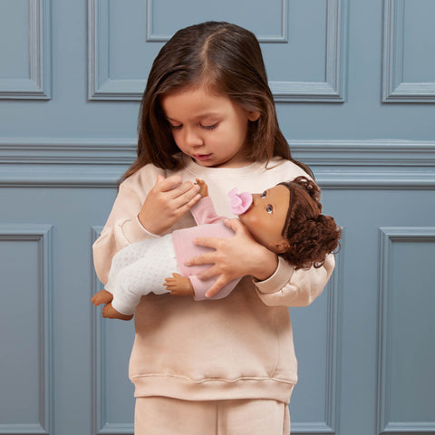 Young girl holding a Lullababy doll against a blue paneled wall