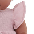 Close-up of a Lullababy 14" Outfit doll dressed in a light pink dress with ruffled sleeves. The doll has a dark complexion, and only the lower part of its face, shoulder, and upper torso are visible. The texture and detailing of the fabric are clearly shown.