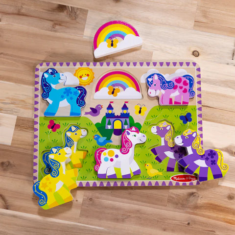 Flat lay of the Melissa & Doug Unicorn Chunky Puzzle with the rainbow piece lifted out above the board, showing all five unicorns in place