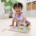 Child playing with the Melissa & Doug Unicorn Chunky Puzzle on the floor, holding the blue unicorn piece with the pink unicorn pieces set aside