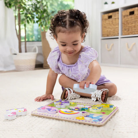 Child playing with the Melissa & Doug Unicorn Chunky Puzzle on the floor, holding the blue unicorn piece with the pink unicorn pieces set aside