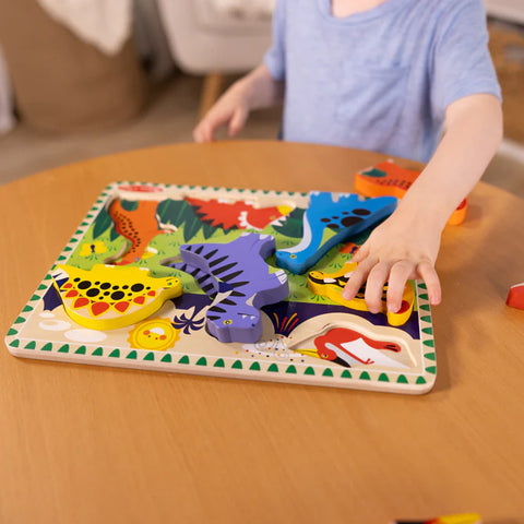 Child playing with the Melissa & Doug Chunky Dinosaur Puzzle at a table, picking up the dinosaur pieces from the board