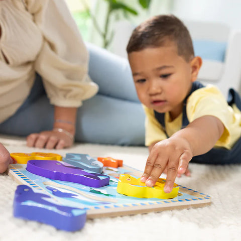 Close-up of a toddler placing the yellow seahorse piece into the Melissa & Doug Sea Life Chunky Puzzle board