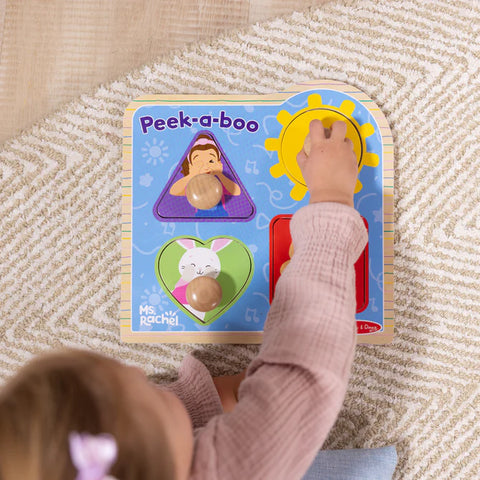 Child playing with a 'Peek-a-Boo' toy on a textured surface