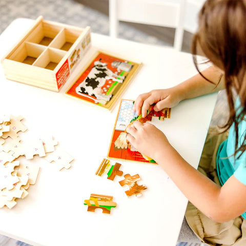 Child assembling one of the Melissa & Doug Farm Puzzles at a table, with the wooden storage box and puzzle pieces spread out nearby