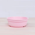 A pink plastic Re-Play Bowl from our vibrant REPLAY tableware set sits empty on a light wooden countertop with a white tile backsplash. The bowl has a simple, smooth design, and its muted pastel color contrasts subtly with the light background, making it both safe for kids and environmentally friendly.