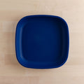 A REPLAY Re-Play Flat Plate, characterized by its square shape, deep blue color, and crafted from recycled materials, is placed on a light wooden surface. The plate features smooth, rounded edges and a minimalist design, exemplifying sustainable tableware at its finest.