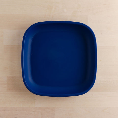 A REPLAY Re-Play Flat Plate, characterized by its square shape, deep blue color, and crafted from recycled materials, is placed on a light wooden surface. The plate features smooth, rounded edges and a minimalist design, exemplifying sustainable tableware at its finest.