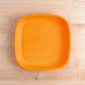 The Re-Play Flat Plate by REPLAY, an orange plastic plate made from recycled materials with slightly rounded corners and a smooth, flat base, rests on a light wood surface that displays a natural grain pattern.