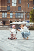 A parent crouching beside a toddler learning to scoot on the Scoot & Ride Highwaykick 1 Push & Go, push bar attached