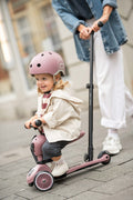 Close-up of a toddler smiling while riding the Scoot & Ride Highwaykick 1 Push & Go in Wildberry, wearing a helmet