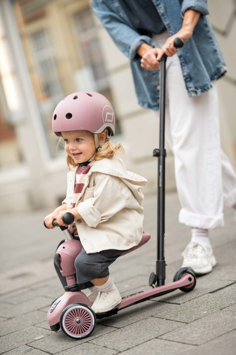 Close-up of a toddler smiling while riding the Scoot & Ride Highwaykick 1 Push & Go in Wildberry, wearing a helmet