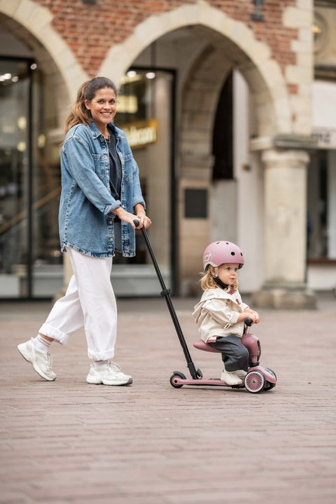 A parent using the push bar to guide a toddler riding the Scoot & Ride Highwaykick 1 Push & Go outdoors