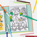 A coloring book page from the Tiger Tribe Colouring Set - Zoo by TIGER TRIBE shows two monkeys in a tree, one holding a banana. Colored markers and a children's book featuring a lion on the cover are nearby. Some parts are colored green, and the background features turquoise polka-dot paper. Perfect for kids' creative play!