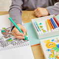 A child coloring in a book featuring a picture of an owl and leaves uses a green marker from their Tiger Tribe Colouring Set - Zoo by TIGER TRIBE, with a variety of colorful markers nearby. The scene includes the set's decorative box adorned with animal illustrations, perfect for kids' creative play.