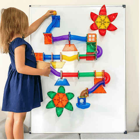 A child building the TileTek Ball Run on a magnetic wall board with flower-shaped tiles
