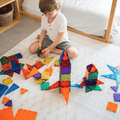Child building a TileTek magnetic tile rocket on the floor beside loose tile pieces